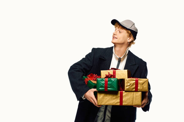 Стильный мужчина уверенно стоит, держа в руках несколько красиво завернутых подарков, украшенных лентами. Одетые в современный праздничный наряд.