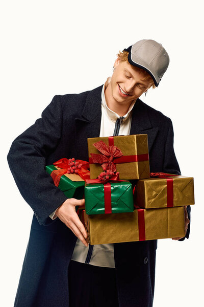 В веселой атмосфере, человек, одетый в модную праздничную моду, радостно несет стопку красиво упакованных рождественских подарков.