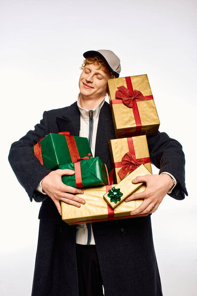Мужчина демонстрирует современную праздничную моду, радуясь нося стопку красиво обернутых подарков.