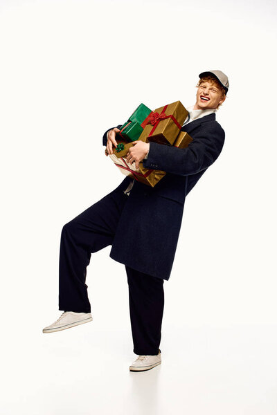 Одетый в модный ансамбль, мужчина радостно балансирует стопку красочных рождественских подарков.