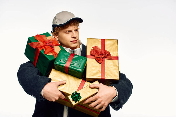 Модный человек уверенно стоит, держа стопку красиво завернутых подарков в праздничные цвета.