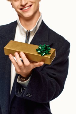 Dressed in stylish holiday attire, a man joyfully holds a beautifully wrapped gift adorned with a green bow. clipart