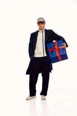 A man showcases a trendy holiday outfit, wearing a long coat and casual attire. He holds a beautifully wrapped gift with a red ribbon, embodying the spirit of Christmas 2025. clipart