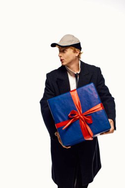 Sıradan tatil kıyafetleri giymiş şık bir adam canlı kırmızı bir fiyonkla süslenmiş büyük mavi bir hediye tutar. Noel 'in neşeli ruhu, kutlamalara hazırlanırken yakalanıyor..