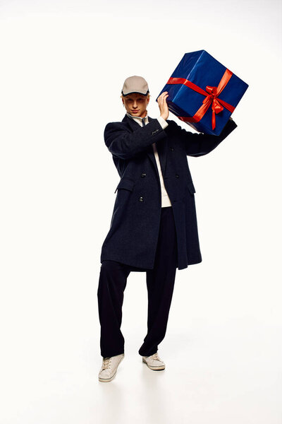 A fashionable man is celebrating the holiday season by playfully holding a large, beautifully wrapped gift adorned with a red ribbon.