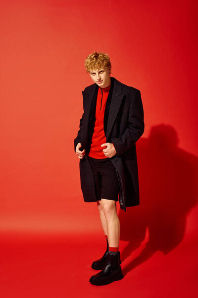 A stylish man poses confidently in vibrant holiday attire, featuring a striking red ensemble complemented by a classic coat. This dynamic look reflects modern fashion trends for Christmas 2025.