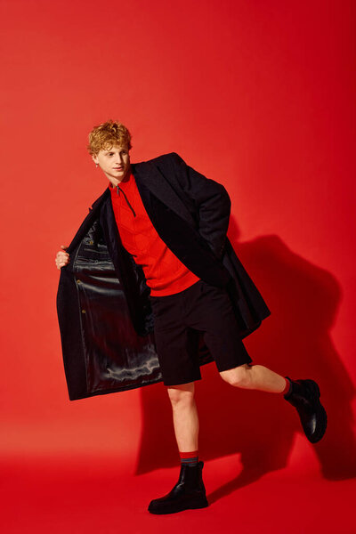 A man poses confidently against a vibrant red backdrop, showcasing a festive holiday outfit.