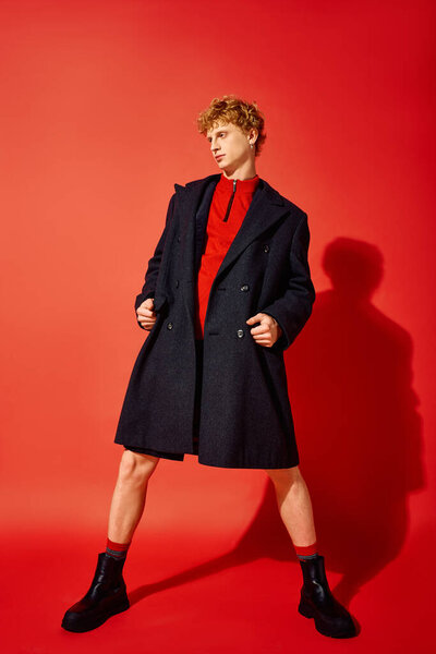 During the Christmas season of 2025, a fashionable man poses confidently in a bold red sweater and striking overcoat. The vivid background enhances his chic look, embodying festive style.