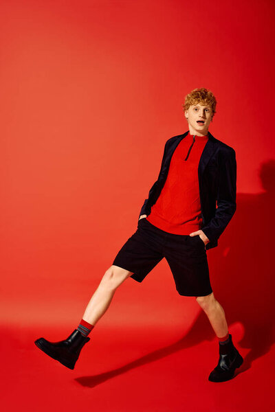 Sporting a striking holiday ensemble, a man with curly hair poses confidently in a vivid red setting.