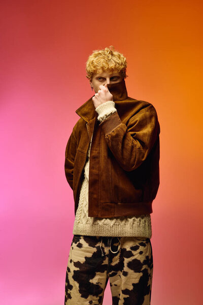 Стильный мужчина представляет поразительный праздничный вид с текстурированной коричневой курткой и узорчатыми брюками на ярком фоне.