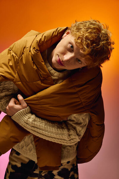 Стильный мужчина в уютном коричневом фугу демонстрирует современную праздничную моду на ярком фоне.