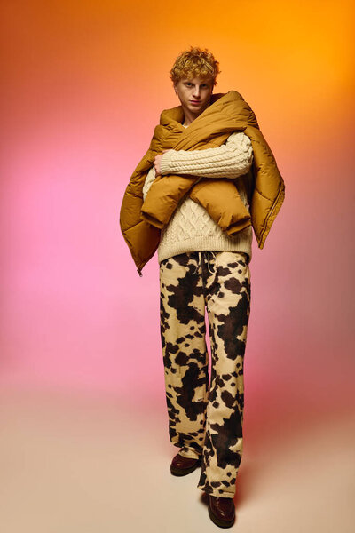 A stylish man showcases a daring Christmas outfit featuring a knitted sweater and striking cow print pants.