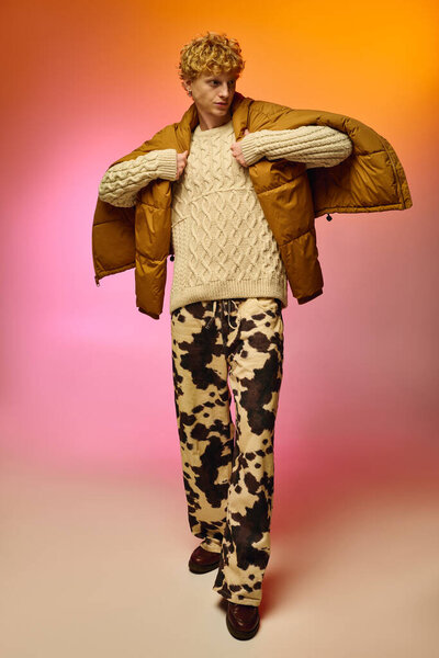 Модный мужчина уверенно позирует, демонстрируя уникальный праздничный наряд с уютным свитером и яркими брюками на ярком фоне. Этот творческий взгляд захватывает дух Рождества 2025 года.