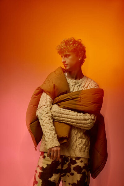 Мужчина демонстрирует модный праздничный наряд с уютным свитером и теплым внешним слоем, источая современный шарм с игривыми узорами. Смелые цвета усиливают праздничный дух,.