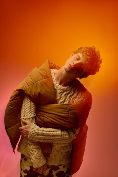 A stylish man showcases a creative holiday outfit featuring a cozy sweater and an eye catching quilted jacket.