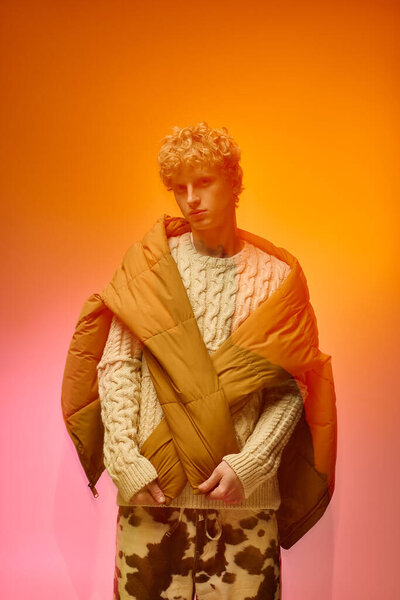 Молодой человек демонстрирует новейшую праздничную моду в 2025 году, сочетая комфорт и стиль с уютным вязаным свитером и крупногабаритным платьем. Теплое освещение усиливает праздничную атмосферу.