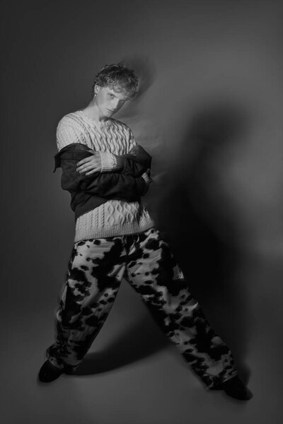 Мужчина демонстрирует инновационный праздничный наряд с текстурированным свитером и жирными штанами для печати коровы. Этот стильный вид отражает тенденции современной моды на Рождество 2025 года.