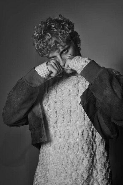 Молодой человек представляет элегантный праздничный наряд. Он имеет стильный вязаный свитер в паре с шикарной курткой, захватив суть праздничной моды.