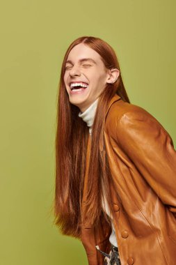 Uçan kızıl saçlı genç bir adam neşeli yeşil bir arka plana gülüyor..
