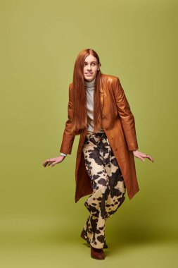 Uzun kızıl saçlı genç bir adam modaya uygun giyinirken duygularını sergiler..