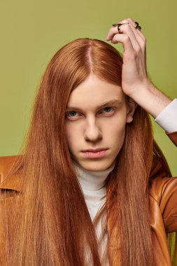 Uzun kızıl saçlı genç adam derin duygular ifade ediyor. Şık kıyafetler ve canlı bir ortam..