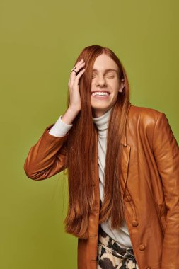 Kahverengi deri ceketli, kırmızı saçlı, duygusal bir adam parlak bir şekilde gülümsüyor..