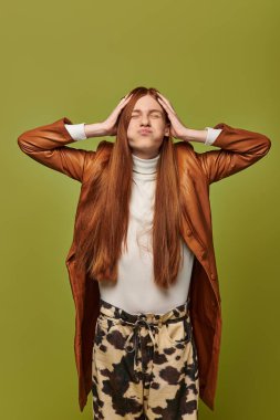 Şık giyinmiş genç adam, yeşil arka planda poz verirken derin duygular sergiliyor..