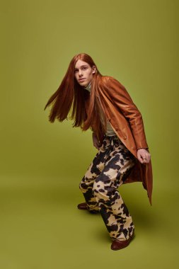 Uzun kızıl saçlı duygusal genç adam canlı yeşil bir arka planda yaratıcı bir şekilde poz veriyor..