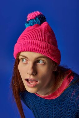 Uzun kızıl saçlı genç bir adam renkli bir bere giyerken şaşırmış bir ifade sergiliyor..