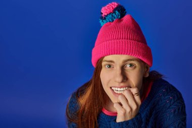 Young man with long red hair smiles warmly while wearing a colorful winter hat and sweater. clipart