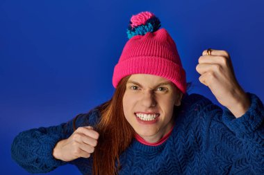 A young man displays intense emotions with clenched fists while wearing a colorful hat. clipart