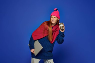 Emotional young man with long red hair holds a coffee cup, smiling in a colorful backdrop. clipart