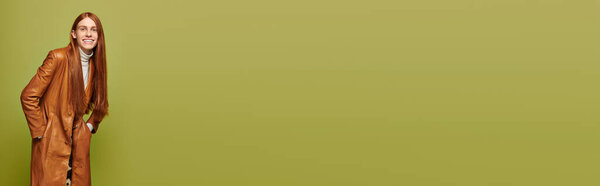 Молодой человек с длинными рыжими волосами уверенно стоит, демонстрируя свои эмоции в яркой обстановке.