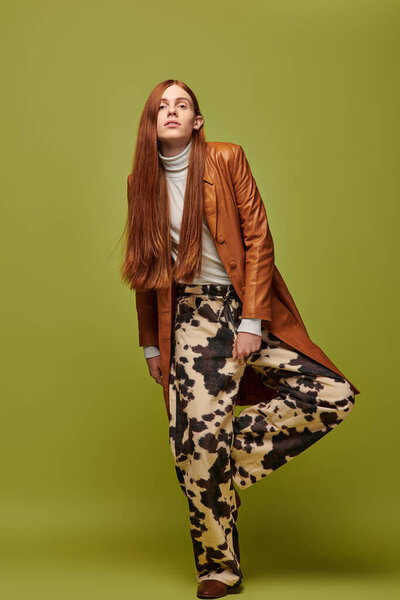 Молодой человек с длинными рыжими волосами демонстрирует сильные эмоции в стильной одежде.