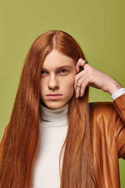 Young man with long red hair shows intense emotions while posing against a vibrant green wall.