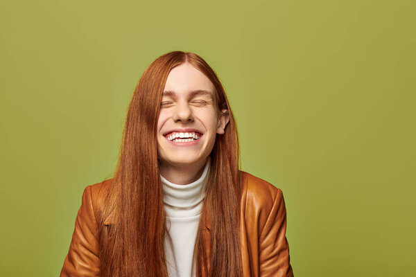 Молодой человек с длинными рыжими волосами выражает радость и тепло, счастливо улыбаясь..