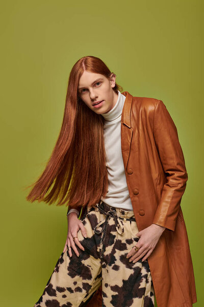 Молодой человек с яркими длинными рыжими волосами демонстрирует глубокие эмоции, позируя творчески.