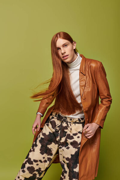 Молодой человек с длинными рыжими волосами демонстрирует свои эмоции в стильной одежде.
