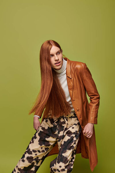 A young man with striking long red hair showcases his emotional expression in a vibrant setting.