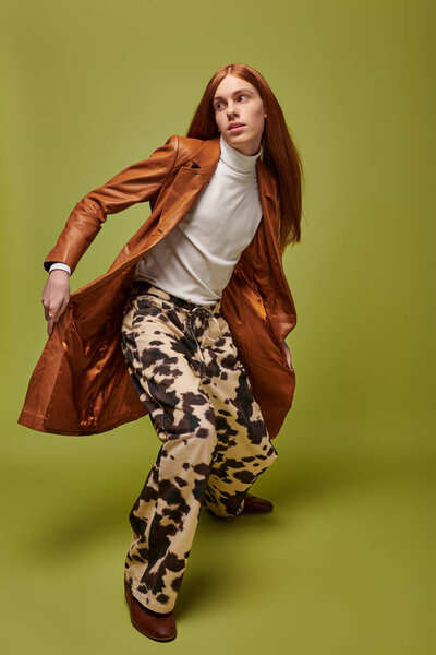 Emotional young man with long red hair poses dramatically in a lively green environment.