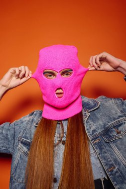 Uzun kızıl saçlı genç bir adam pembe bir maske takıyor..