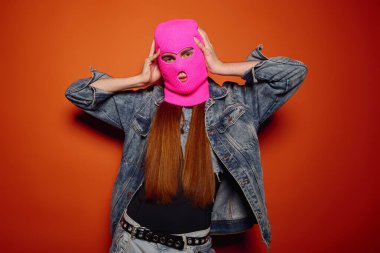 Young man showcases strong emotions while wearing a bright ski mask against an orange backdrop. clipart