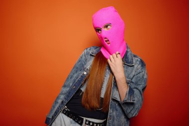 Uzun kızıl saçlı genç adam pembe bir maske takarken derin duygular ifade eder..