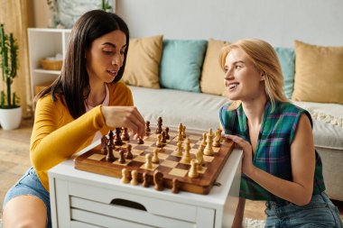 Two young women share a playful moment while playing chess in their bright living space. clipart