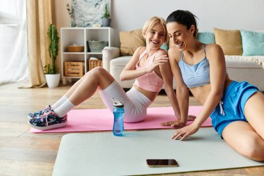 İki kadın evde yoga minderleri üzerinde çalışırken aynı kahkahayı ve sevgiyi paylaşıyor..