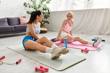 Güneşli bir odada yoga minderleri üzerinde gerinirken iki genç kadın aynı şefkatli anı paylaşıyor..