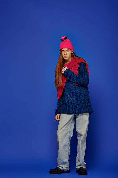 Young man with long red hair shows deep emotions while standing in colorful fashion.