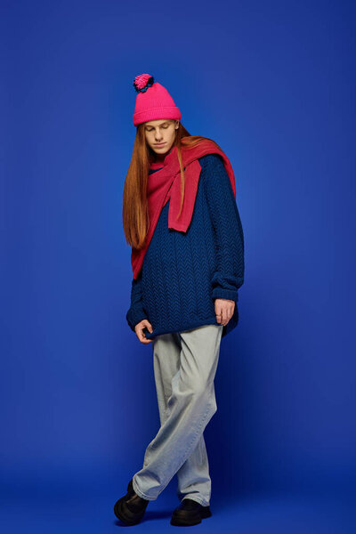 Emotional young man with long red hair stands thoughtfully in colorful attire, embracing calmness.