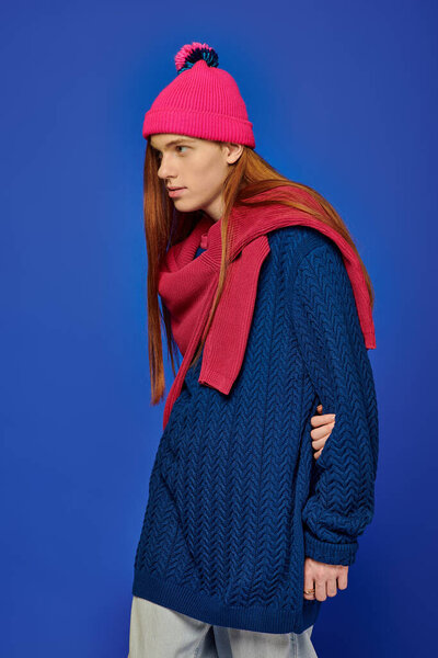 A young man with long red hair shows deep emotions while wearing cozy winter clothing.