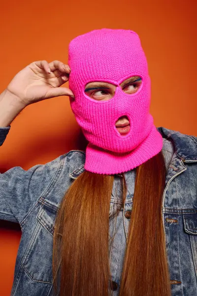 Genç adam, turuncu bir arka plana parlak pembe bir maske takarak derin duygular ifade ediyor..
